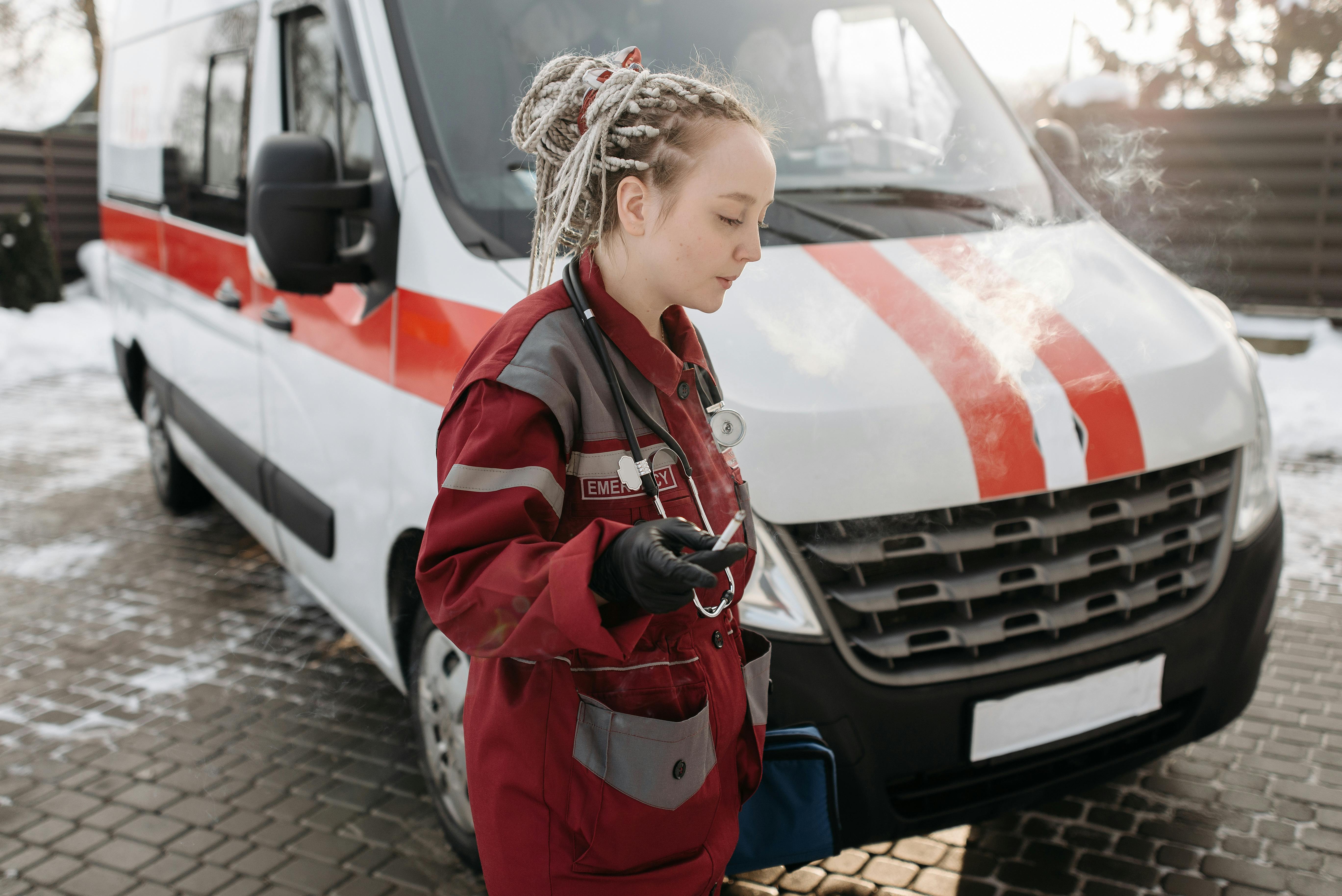 A woman paramedic taking a smoke break beside an ambulance on a snowy winter day.