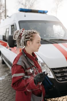 A female paramedic in uniform prepares for duty outside an ambulance.