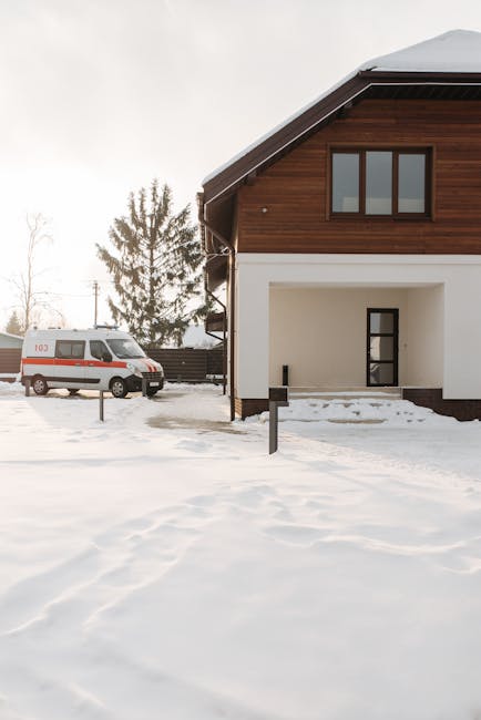 A peaceful winter scene with a house and ambulance parked on a snowy driveway.