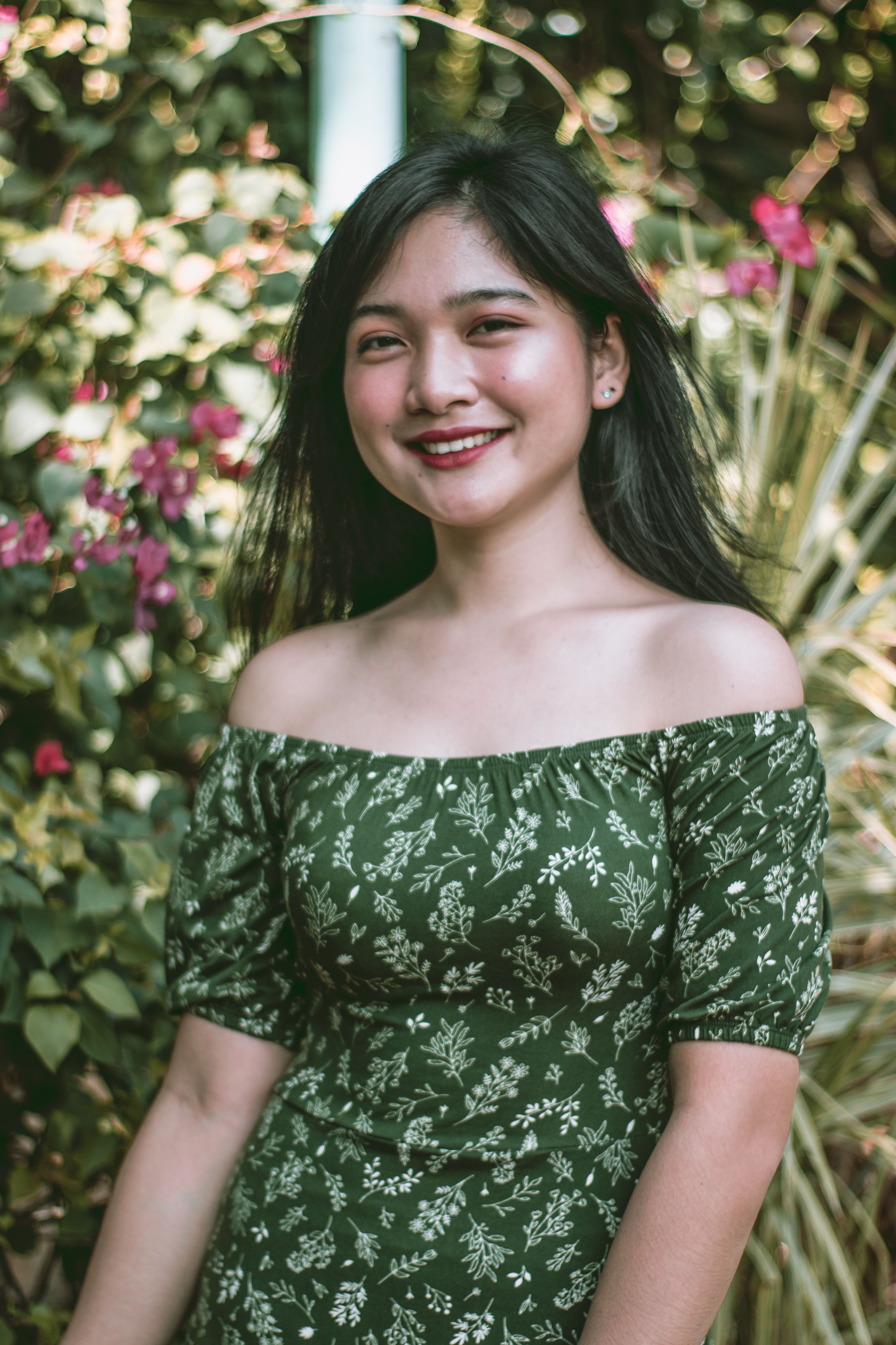 A young Asian woman smiling in a floral dress, surrounded by greenery, capturing a lively and natural moment.