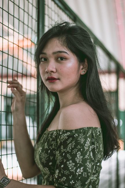 A captivating portrait of an adult woman standing by a metal fence indoors.