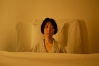 Woman in Gray Button Up Shirt Sitting on White Bed