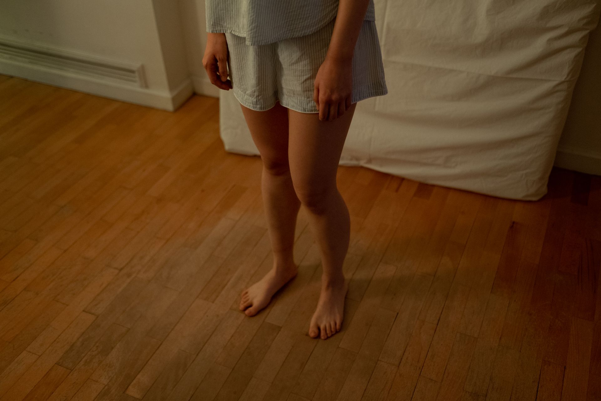 A Person in Blue Shorts Standing Barefooted on a Wooden Floor