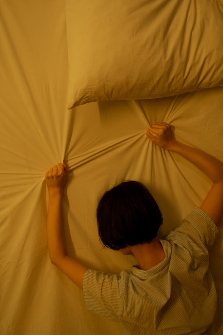 A Woman Gripping The Blanket On Bed