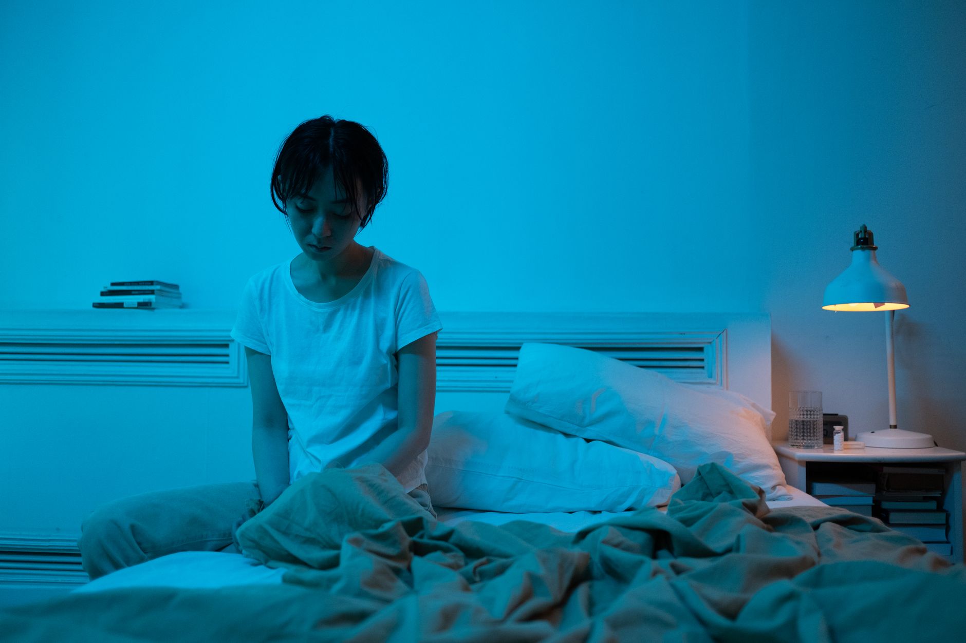 11 hábitos que pioram a depressão, e o que eu faço no lugar 4 A woman sits in a blue lit room reflecting loneliness and introspection.
