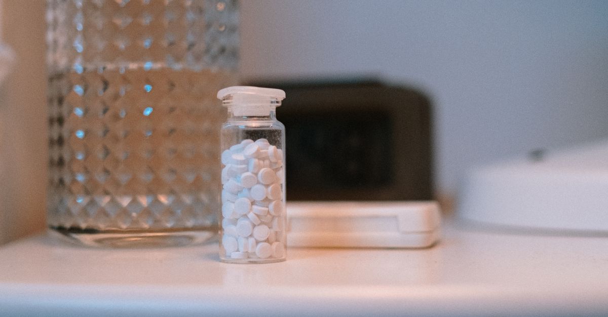 A clear glass bottle with white pills beside a glass of water