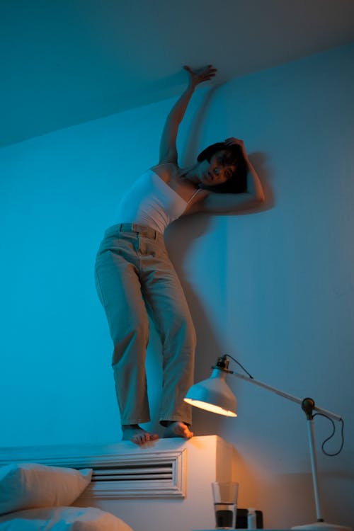 A Woman Standing on the Bed while Touching the Ceiling