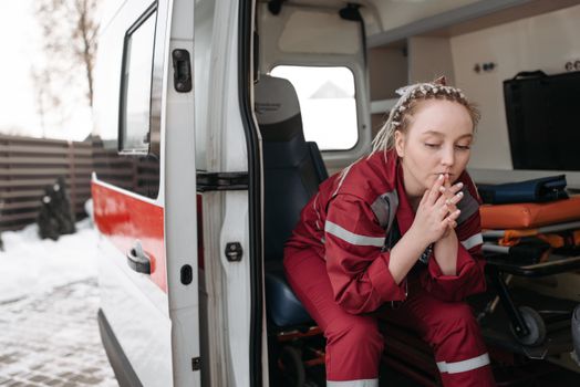 A female paramedic sits pensively beside an ambulance, reflecting on duty.