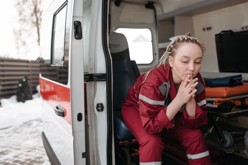 Free A female paramedic sits pensively beside an ambulance, reflecting on duty. Stock Photo