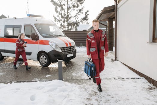 Paramedics in red uniforms responding to an emergency with an ambulance in snowy conditions.