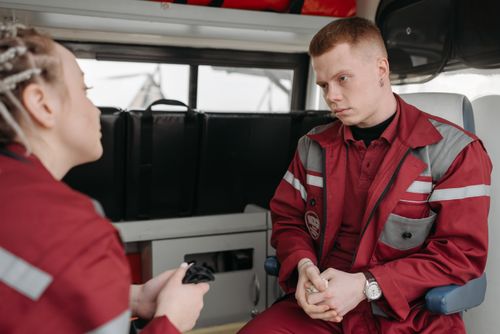 Free Two EMTs in burgundy uniforms engaged in serious conversation inside an ambulance. Stock Photo