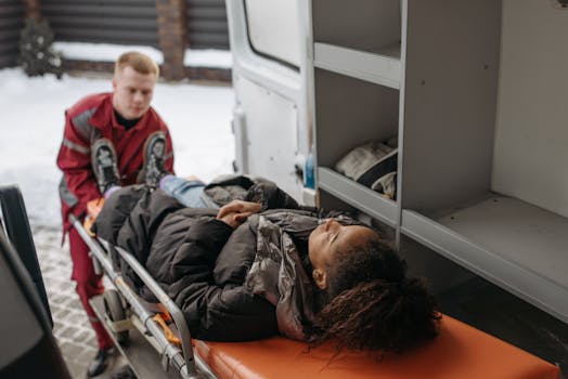 Emergency medical technicians assisting a patient onto a stretcher and into an ambulance.