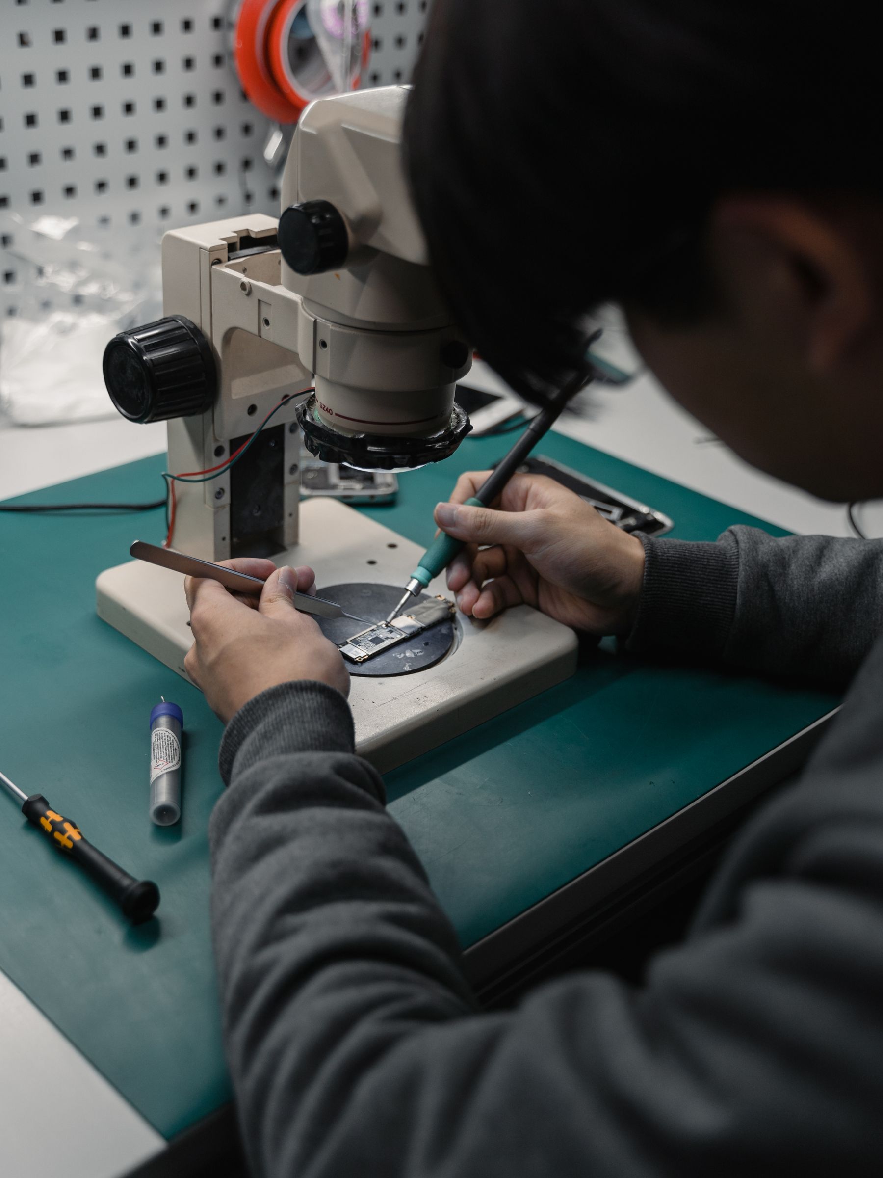 LAP CURE technician performing chip-level laptop motherboard repair under a microscope with precision soldering tools
