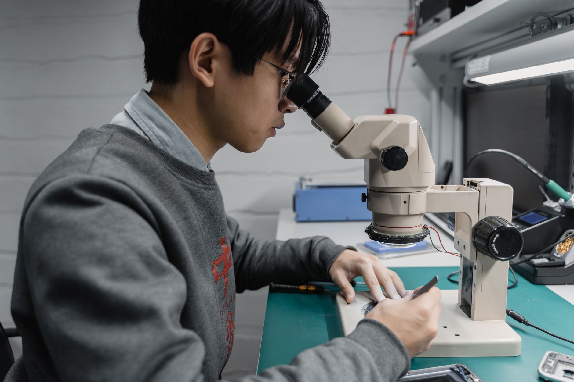 Young male technician working with a microscope in a laboratory setting, focused on electronics.
