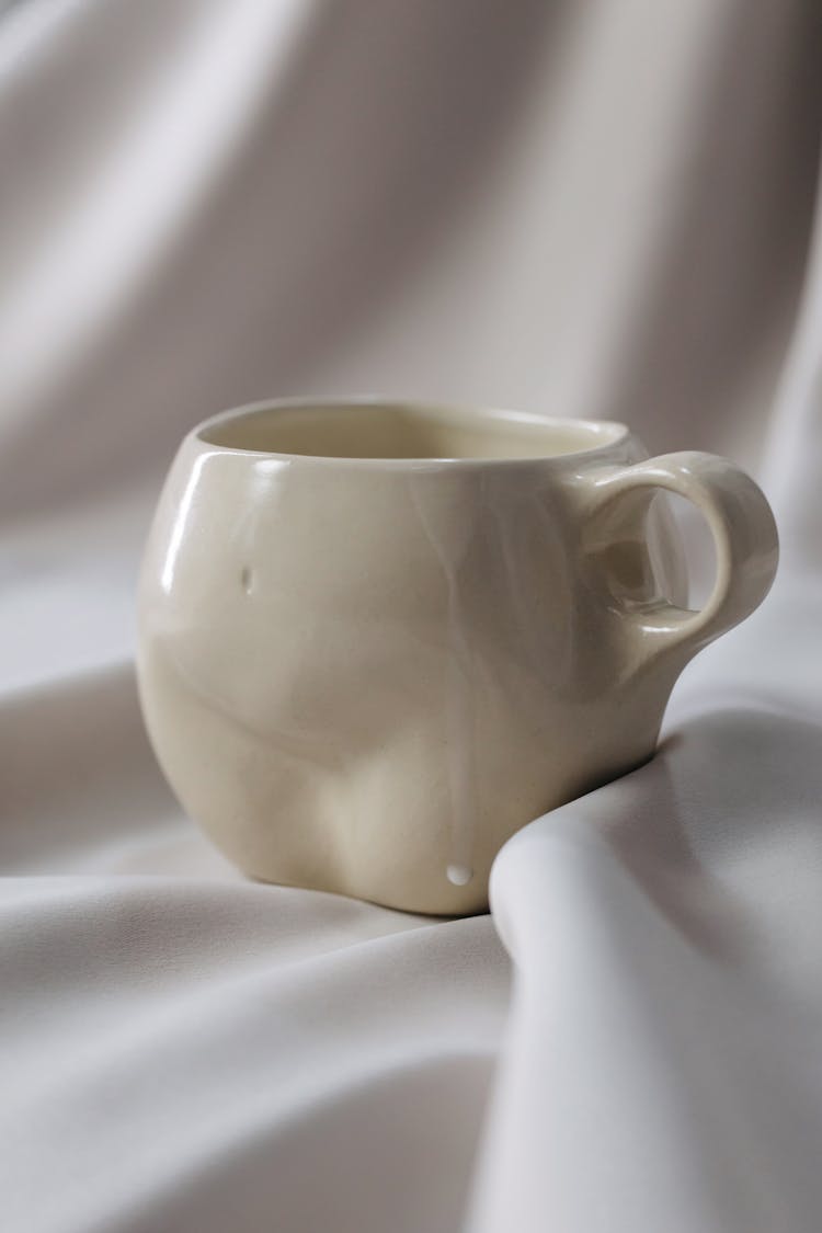 A White Ceramic Cup On White Textile