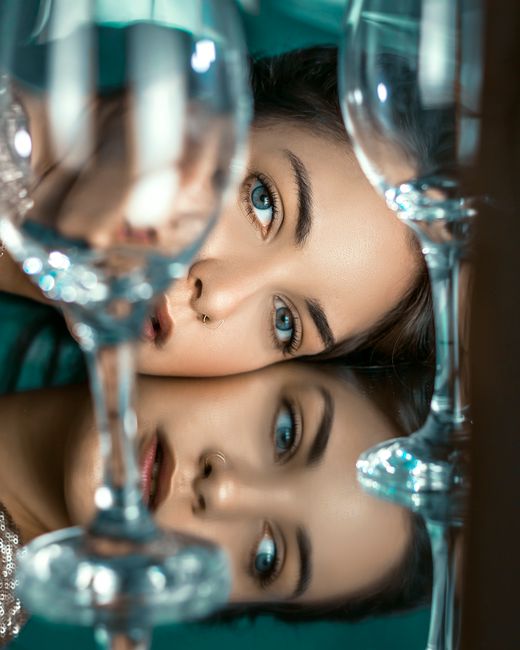 Artistic portrait of a woman with blue eyes, reflecting through wine glasses.