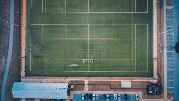Aerial view of distant unrecognizable people standing on green grassy rugby field on sunny day