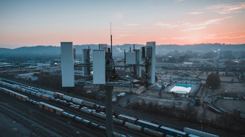 Free Drone view of contemporary cell tower located near railway tracks with cargo containers and wagons against sunset sky Stock Photo