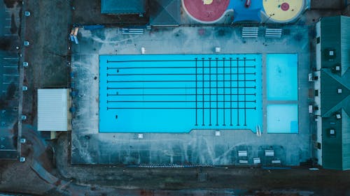 Aerial view of empty outdoor swimming pool and small house located in suburban area of city in daytime