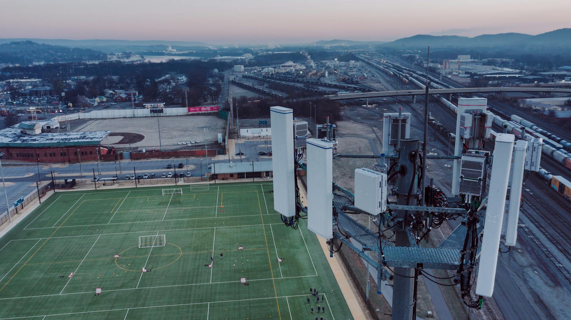 Drone view of contemporary cell site with antennas located in city suburb near green rugby fields against sundown sky in Chattanooga