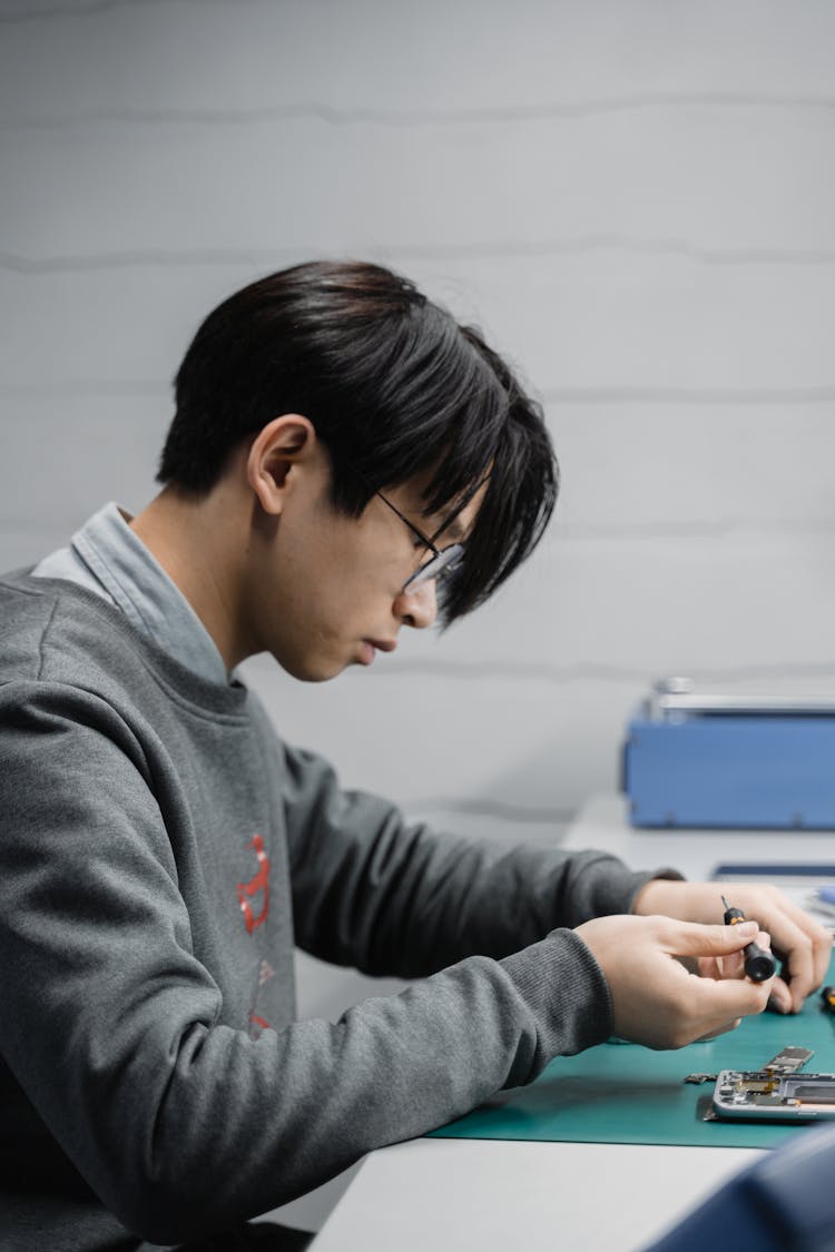 Side View Shot Of A Man Repairing The Broken Cellphone On The Table