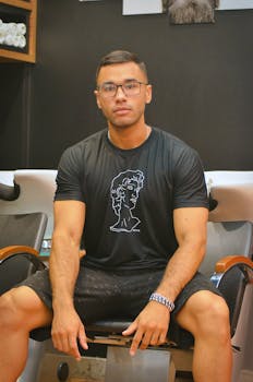 Confident young man wearing eyeglasses sitting on a chair in a modern barbershop.