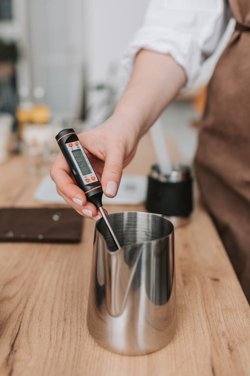 Person Holding Thermometer in Metal Mug