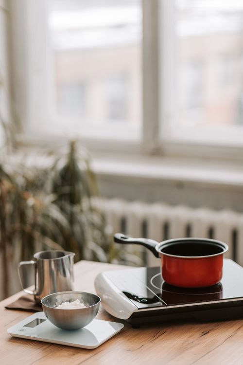 Red pot cooking on a portable induction cooker beside a kitchen scale and mug