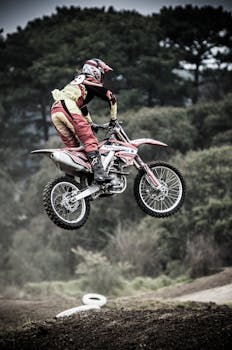 Motorcyclist executing a high jump during an outdoor competition surrounded by nature.