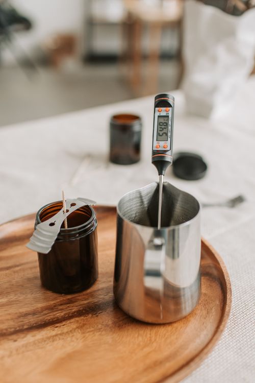 Free Close-up of candle making tools including a pitcher, thermometer, and wick on a wooden tray. Stock Photo