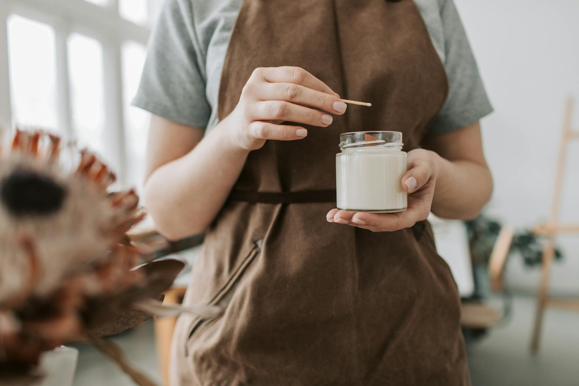 Close-up of an artisan crafting a handmade scented candle in a workshop setting.