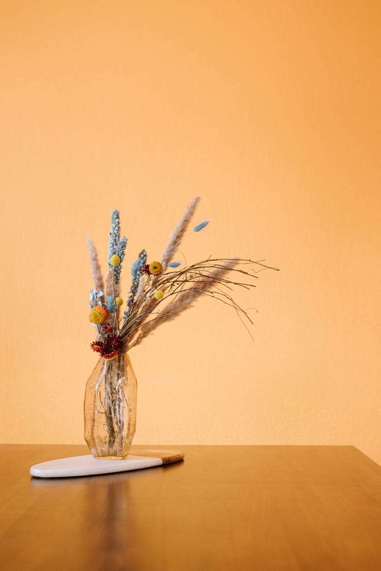 Vase With Plants And Flowers On Table Near Yellow Wall