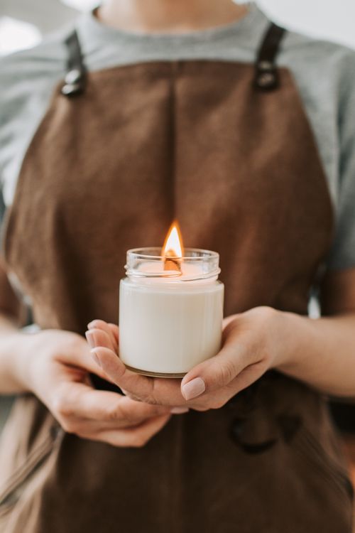 Free Warm ambient lighting with a focus on handmade candle in a jar held by a craftsman wearing an apron. Stock Photo