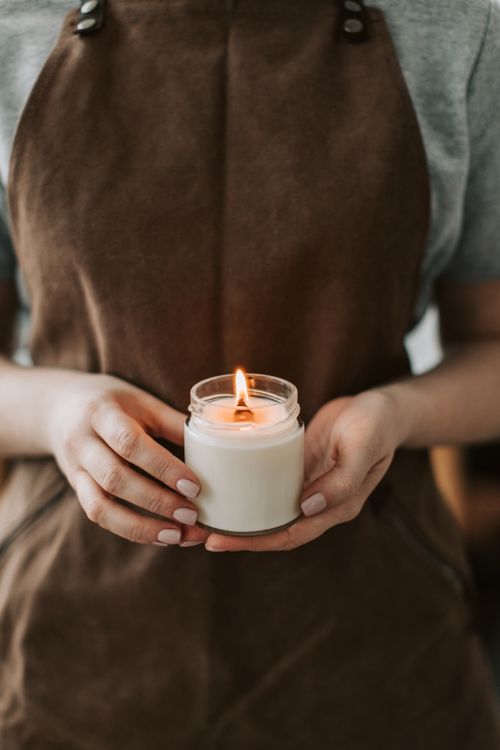 Free Close-up of hands holding a lit candle, wearing a brown apron in a cozy setting. Stock Photo