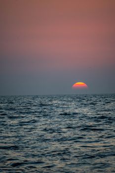 A beautiful sunset over the ocean, showcasing a pink sky and tranquil waves.