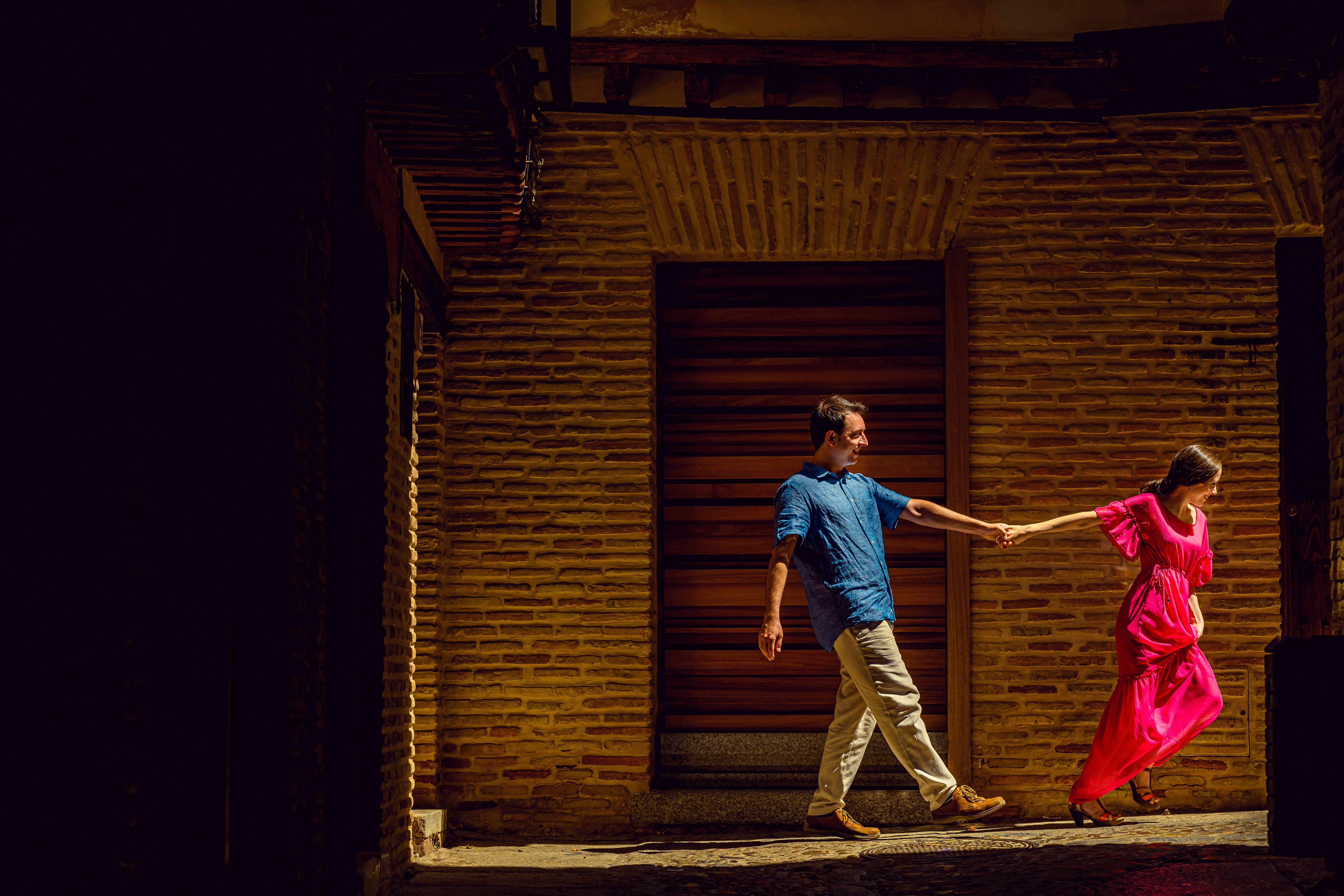 A couple holding hands while walking through the charming streets of Toledo, Spain in warm daylight.