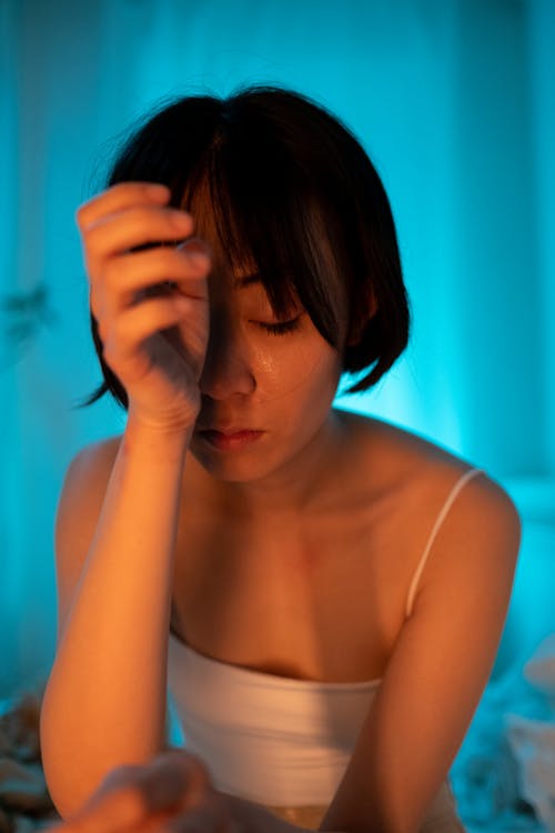 Free A Short Haired Woman in White Tank Top with Her Hand on Her Face Stock Photo