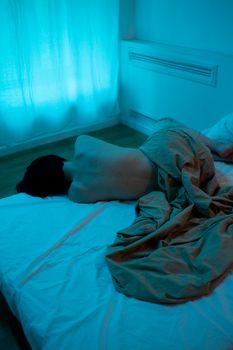 A person lies on a bed in a dimly lit, moody room, evoking solitude and tranquility.