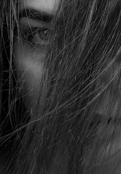 Black and white close-up portrait of a woman with hair covering her face, expressive eye visible.