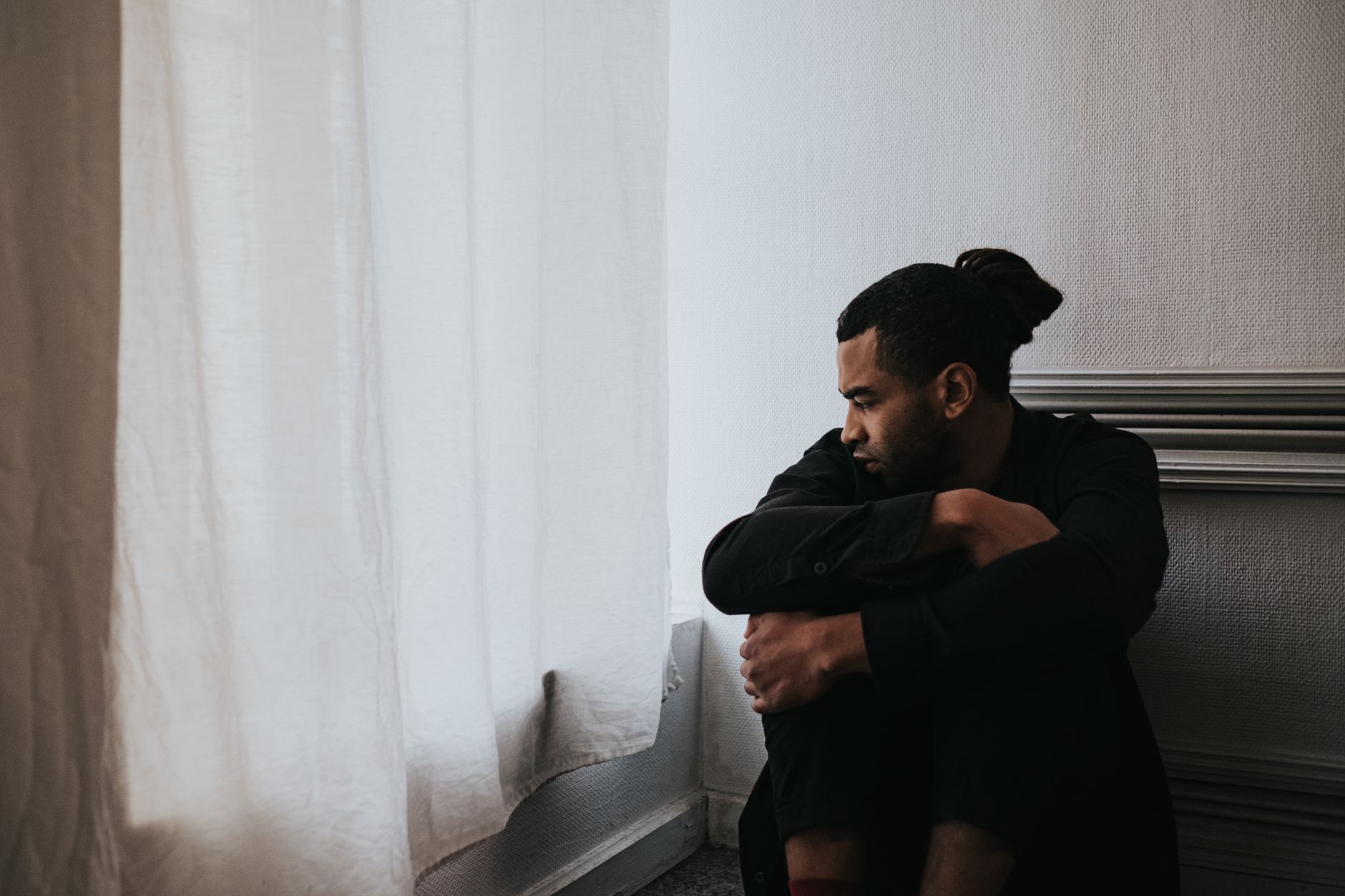 A man sits alone by a window, reflecting on emotions in a minimalist room.