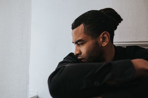 Free Man with dreadlocks sits indoors in deep thought and solitude. Stock Photo