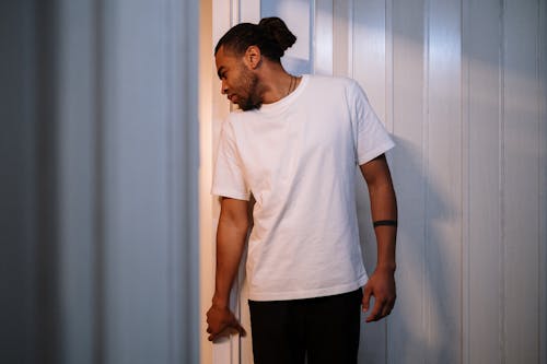 Man in White Crew Neck T-shirt and Black Pants Standing Beside White Curtain