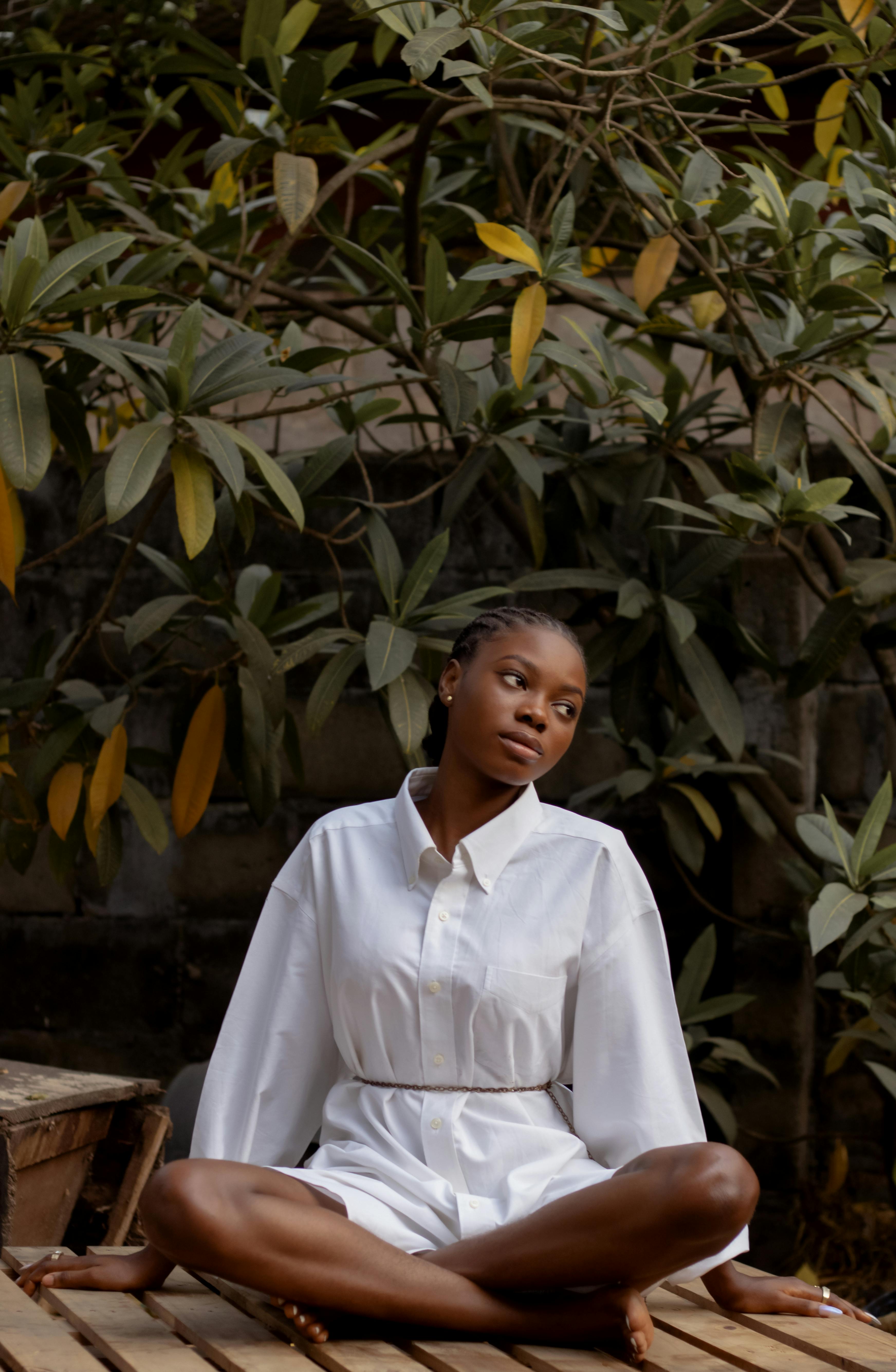 Stylish woman sitting outdoors in a white shirt surrounded by lush greenery.