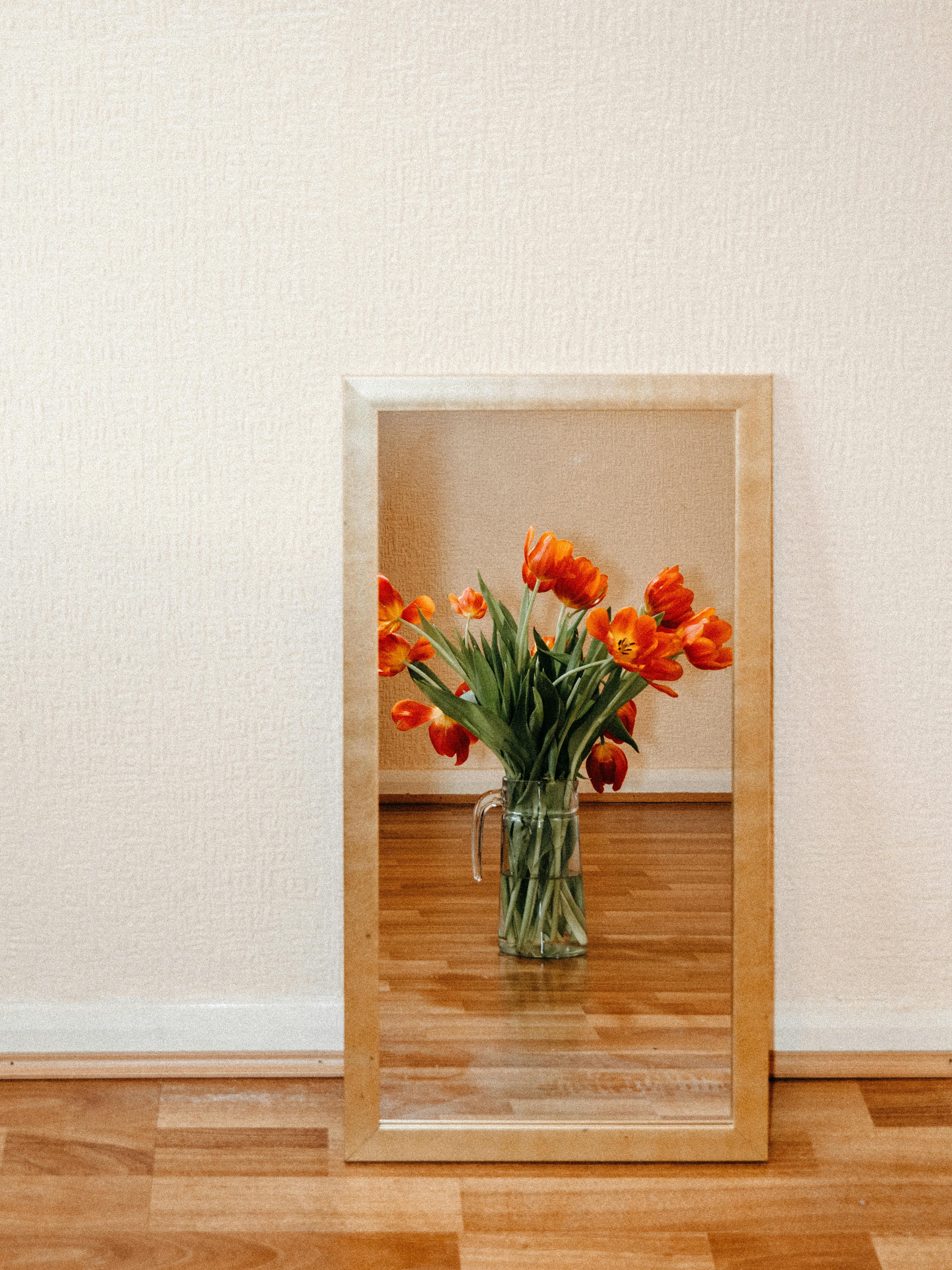 A beautiful bouquet of red tulips in a glass vase, reflected in a wall-mounted mirror against a wooden floor.
