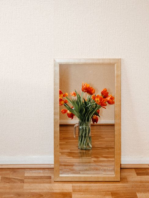 A beautiful bouquet of red tulips in a glass vase, reflected in a wall-mounted mirror against a wooden floor.