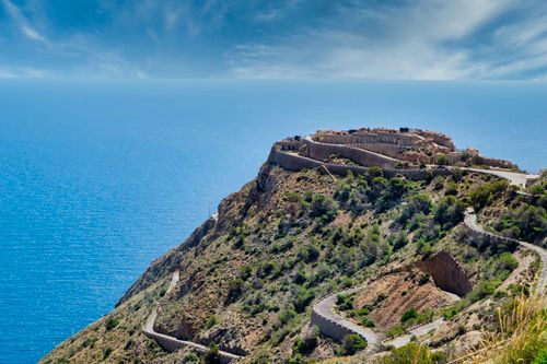 Free A breathtaking view of a historic fortress on a coastal hill overlooking the sea under a bright blue sky. Stock Photo