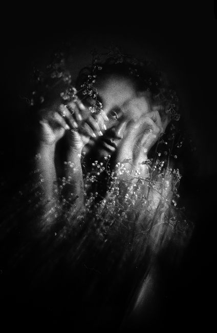 Black and white of young female touching face and looking at camera on black background