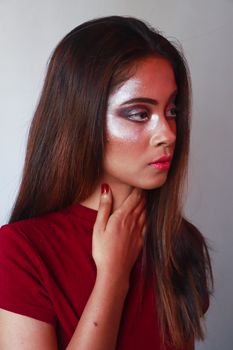 Young female with long hair and red lips touching neck and looking away while standing against gray background