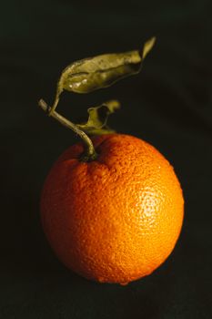 Close-up of a ripe orange with leaf on a dark background, showcasing its vibrant color and texture.