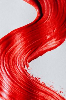 Close-up of a shimmering red brushstroke on white, showcasing texture and abstract art.
